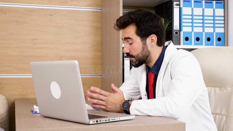 Junger Doktor am Schreibtisch in seinem Büro mit einem Laptop in der Front stock footage