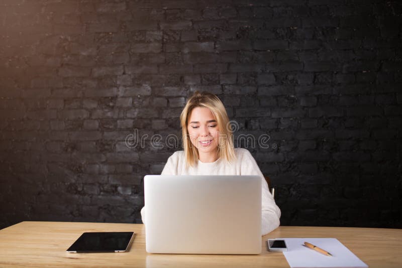 Junger Freiberufler der hübschen Frau, der im Internet auf der Laptop-Computer, sitzend im modernen Innenraum arbeitet stockbild