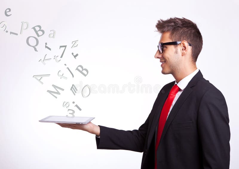 Side view of a young business man holding a touch screen pad and looking up above it at some symbols and words comming out of it. Side view of a young business man holding a touch screen pad and looking up above it at some symbols and words comming out of it