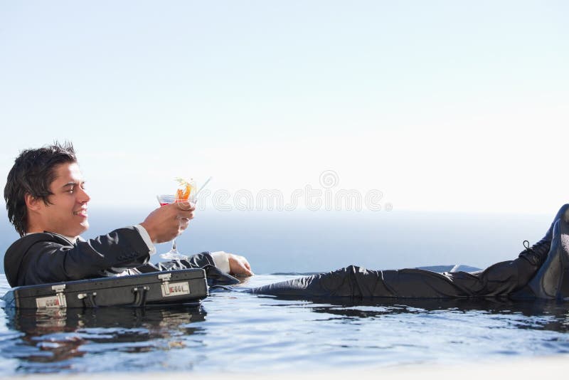 Junger Geschäftsmann, der in einem Swimmingpool mit einem Cocktail sich entspannt lizenzfreie stockfotografie Junger Geschäftsmann, der in einem Swimmingpool mit einem Cocktail sich entspannt lizenzfreie stockfotografie