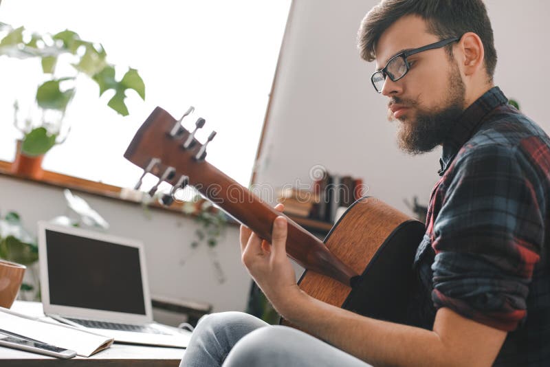 Junger Gitarristhippie zu Hause, der Gitarrenfensterlicht hält lizenzfreie stockfotos Junger Gitarristhippie zu Hause, der Gitarrenfensterlicht hält lizenzfreie stockfotos