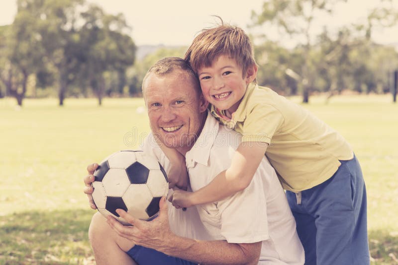 Junger glücklicher Vater und aufgeregte 7 oder 8 Jahre alte Sohn, die zusammen Fußballfußball auf dem Stadtparkgarten aufwirft sü stockfoto Junger glücklicher Vater und aufgeregte 7 oder 8 Jahre alte Sohn, die zusammen Fußballfußball auf dem Stadtparkgarten aufwirft sü stockfoto