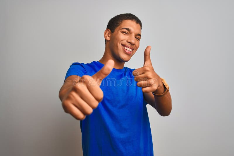 Junger gut aussehender arabischer Mann mit blauem Hemd, der über isoliertem weißem Hintergrund steht und mit der Hand eine positiv. Junger arab Mann mit blauen Hemden, der über isoliertem weißem Hintergrund steht und positive Gesten mit einem lächelnden Handlüm und glücklich für den Erfolg vornimmt. Gewinnergestalt