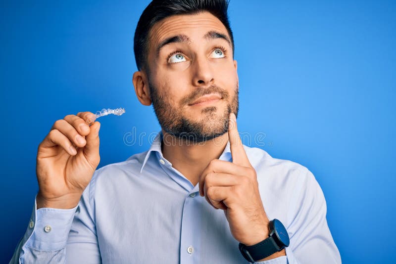 Junger gut aussehender Mann mit zahnärztlicher Zahnkorrektur über blauem Hintergrund seriöses Gesicht, der Fragen sehr ernst nimmt lizenzfreie stockfotos