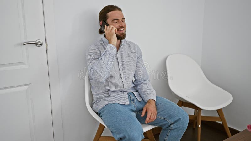 Junger hispanischer Mann, der auf Smartphone sitzt und im Wartezimmer lächelt