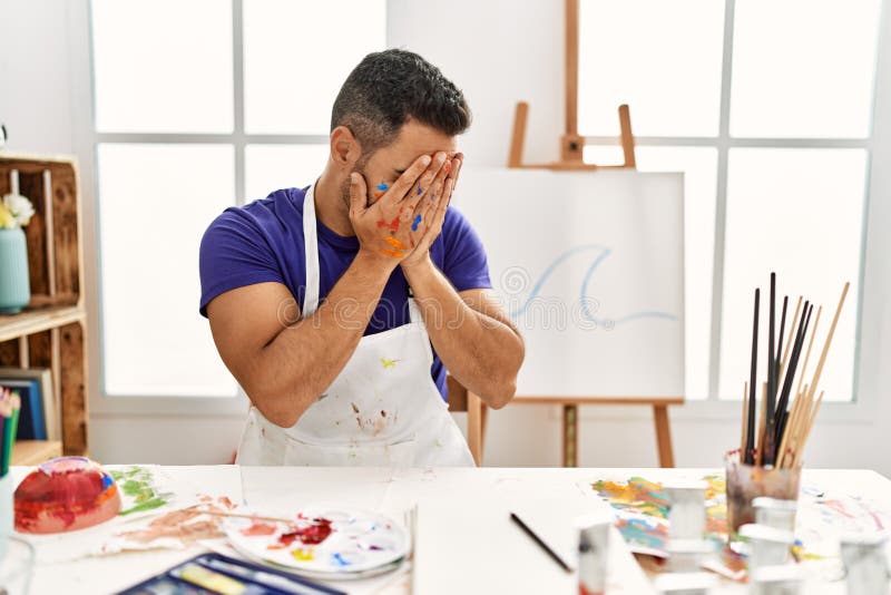 Young hispanic man with beard at art studio with painted face with sad expression covering face with hands while crying. depression concept. Young hispanic man with beard at art studio with painted face with sad expression covering face with hands while crying. depression concept