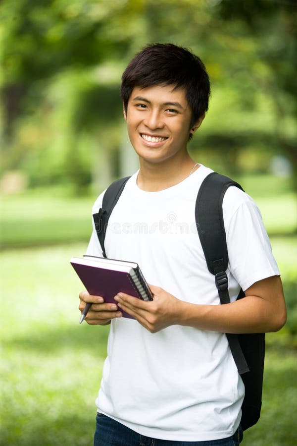 Junger hübscher asiatischer Student mit Büchern und Lächeln in im Freien lizenzfreies stockbild Junger hübscher asiatischer Student mit Büchern und Lächeln in im Freien lizenzfreies stockbild
