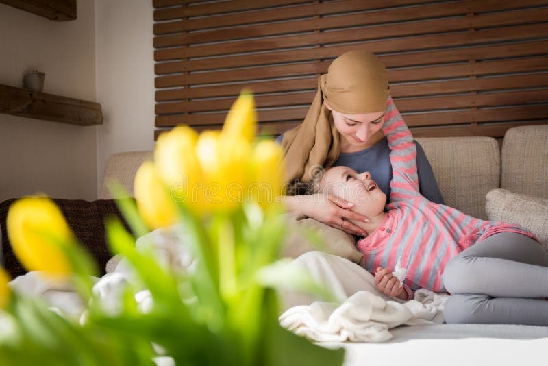 Junger Krebspatient der erwachsenen Frau, der zu Hause Zeit mit ihrer Tochter, entspannend auf der Couch verbringt Krebs und Fami lizenzfreie stockfotografie Junger Krebspatient der erwachsenen Frau, der zu Hause Zeit mit ihrer Tochter, entspannend auf der Couch verbringt Krebs und Fami lizenzfreie stockfotografie