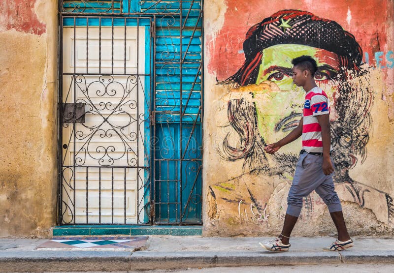 Young cuban man walks by a colorful Che Guevara portrait painted on a shabby old wall in Old Havana. Young cuban man walks by a colorful Che Guevara portrait painted on a shabby old wall in Old Havana