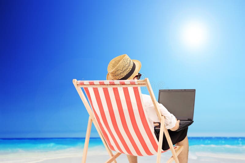 Junger Mann auf einem Stuhl im Freien, der an einem Laptop, nahe bei einem Meer arbeitet stockfotografie Junger Mann auf einem Stuhl im Freien, der an einem Laptop, nahe bei einem Meer arbeitet stockfotografie