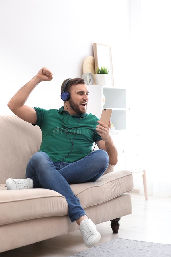 Young man in headphones with mobile device enjoying music on sofa at home. Young man in headphones with mobile device enjoying music on sofa at home