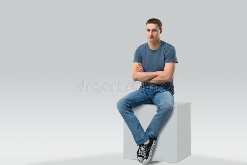 Junger Mann, der auf weißem Würfel sitzt Getrennt lizenzfreie stockfotografie Junger Mann, der auf weißem Würfel sitzt Getrennt lizenzfreie stockfotografie