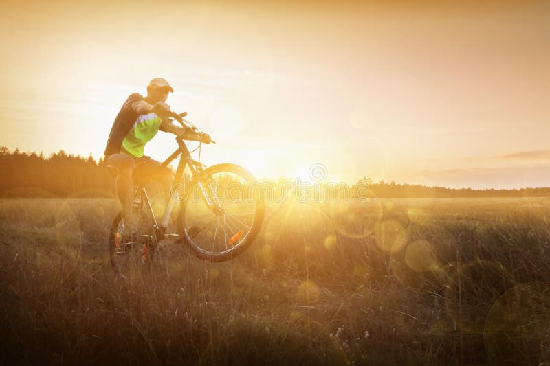 Junger Mann, der ein Fahrrad bei Sonnenuntergang reitet lizenzfreies stockfoto Junger Mann, der ein Fahrrad bei Sonnenuntergang reitet lizenzfreies stockfoto