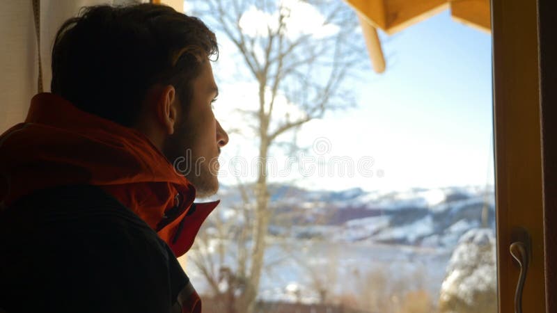 Junger Mann, der heraus das Fenster schöner Landschaft im Winter betrachtet