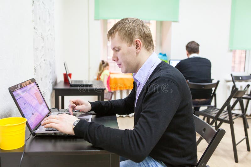 Junger Mann, der im Raum, schreibend auf Laptop sitzt stockbild Junger Mann, der im Raum, schreibend auf Laptop sitzt stockbild
