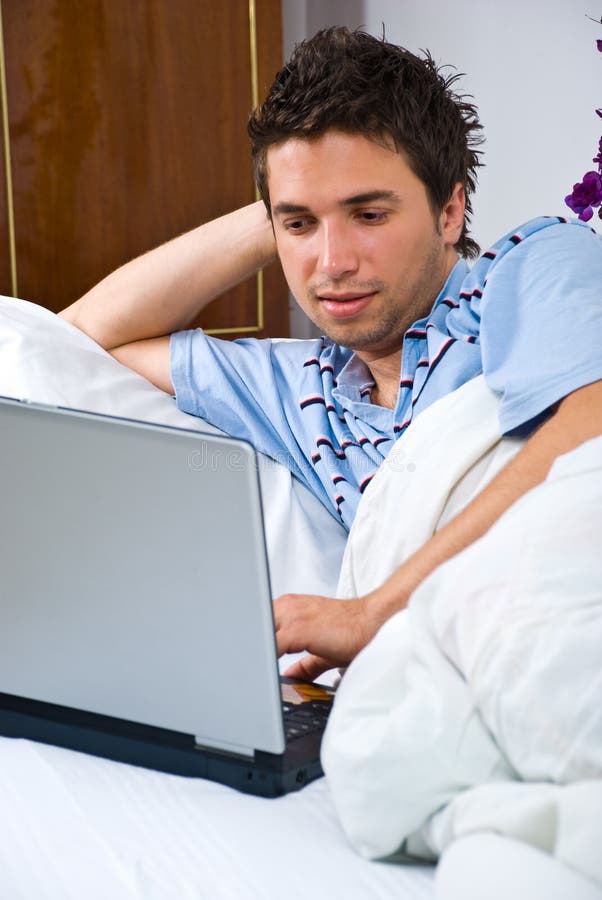 Junger Mann, der Laptop im Bett verwendet lizenzfreie stockfotografie Junger Mann, der Laptop im Bett verwendet lizenzfreie stockfotografie