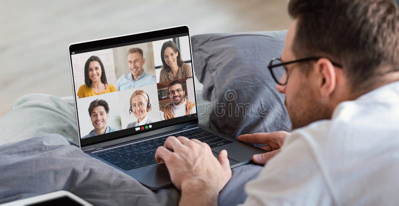 Junger Mann, der on-line-Arbeitssitzung auf dem Notebook zu Hause liegt im Bett und Gruppenvideoanruf mit seinen Mitarbeitern hat stockbild