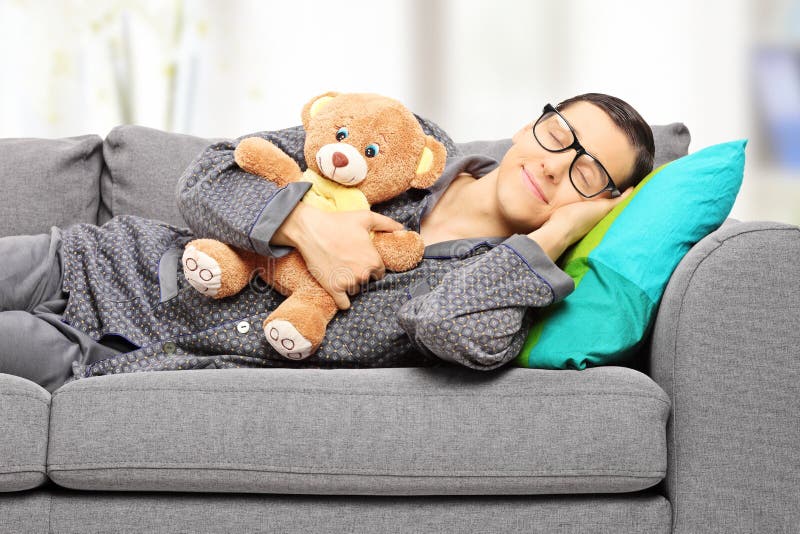 Junger Mann, der Teddybären hält und auf Couch ein Schläfchen hält