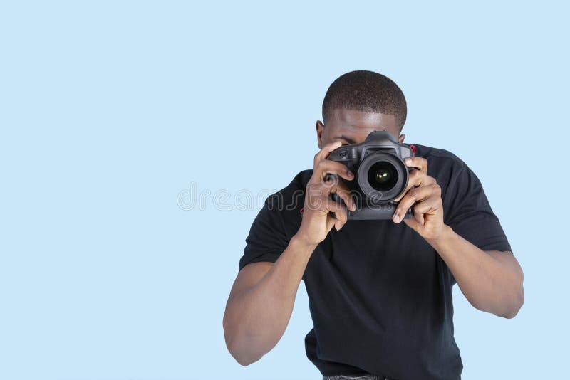 Junger Mann des Afroamerikaners, der Foto durch Digitalkamera über blauem Hintergrund macht lizenzfreies stockfoto Junger Mann des Afroamerikaners, der Foto durch Digitalkamera über blauem Hintergrund macht lizenzfreies stockfoto