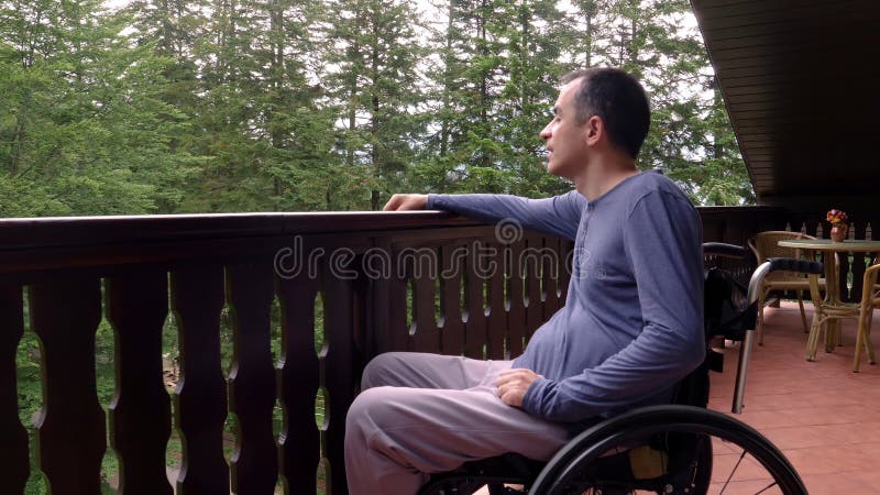 Junger Mann im Rollstuhl, der auf Terrasse sich entspannt stock footage Junger Mann im Rollstuhl, der auf Terrasse sich entspannt stock footage