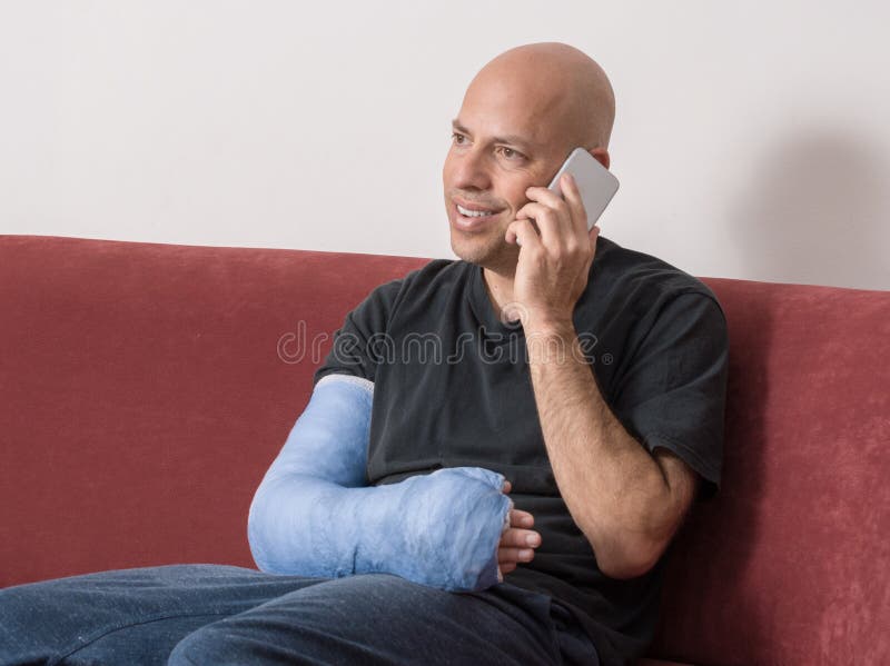 Young man with an arm and elbow in a blue plaster / fiberglass cast at home, happily talking on his phone after having broken his arm. Young man with an arm and elbow in a blue plaster / fiberglass cast at home, happily talking on his phone after having broken his arm