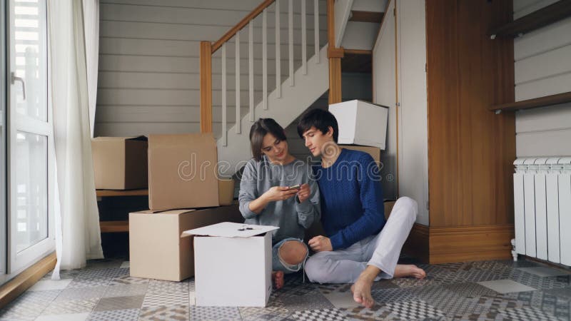 Junger Mann und Frau nehmen selfie mit dem Smartphone, der Herzform mit den Fingern macht, die auf Boden der neuen Wohnung sitzen