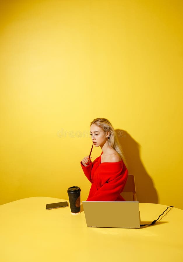 Junger Modem?dchen Blogger gekleidet im stilvollen roten Mantel, der an am gelben Tisch mit dem Laptop und dem Tasse Kaffee sitzt lizenzfreie stockbilder Junger Modem?dchen Blogger gekleidet im stilvollen roten Mantel, der an am gelben Tisch mit dem Laptop und dem Tasse Kaffee sitzt lizenzfreie stockbilder