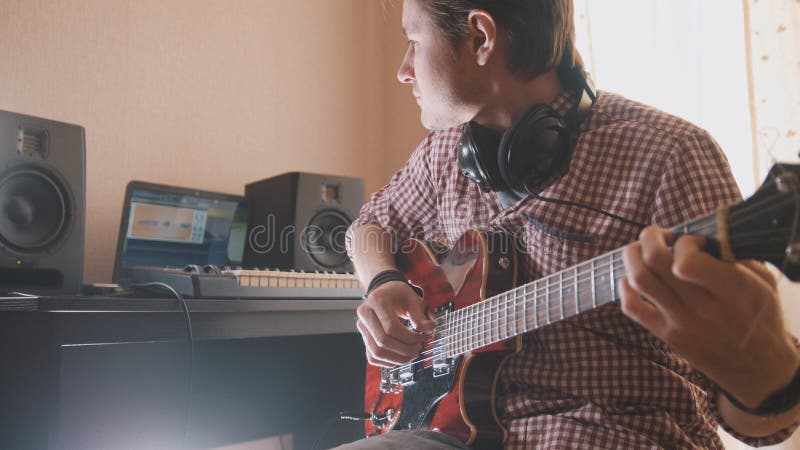 Junger Musiker verfasst und notiert die Filmmusik, welche die Gitarre unter Verwendung des Computers, der Kopfhörer und der Tasta lizenzfreie stockfotografie Junger Musiker verfasst und notiert die Filmmusik, welche die Gitarre unter Verwendung des Computers, der Kopfhörer und der Tasta lizenzfreie stockfotografie