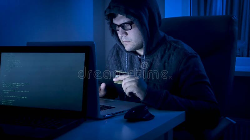 Junger männlicher Hacker in der Haube, die an Laptop arbeitet, um Geld von der Kreditkarte zu stehlen lizenzfreie stockfotografie