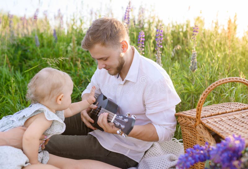 Junger Papa, der bei Sonnenuntergang auf einem Picknick auf einem Feld spielt lizenzfreies stockfoto