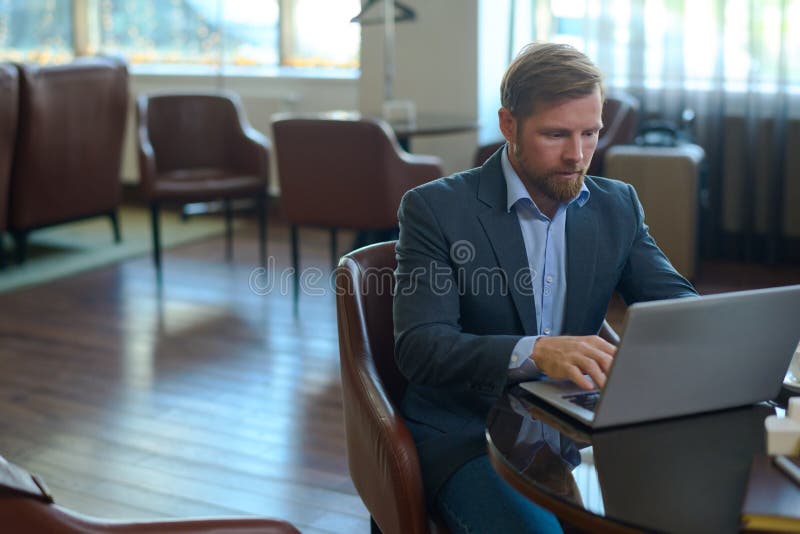 Junger seriöser Geschäftsmann in Formalbekleidung sitzend am Tisch vor dem Laptop stockfoto