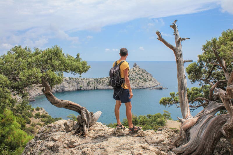 Junger sportlicher Mann mit dem Rucksack, der auf die Oberseite des Felsens steht lizenzfreie stockfotografie Junger sportlicher Mann mit dem Rucksack, der auf die Oberseite des Felsens steht lizenzfreie stockfotografie