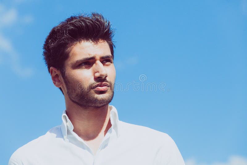 Junger stolzer Mann auf Hintergrund des blauen Himmel Portrait eines gut aussehenden Mannes draußen Modisches Haar und Bart stockfotografie
