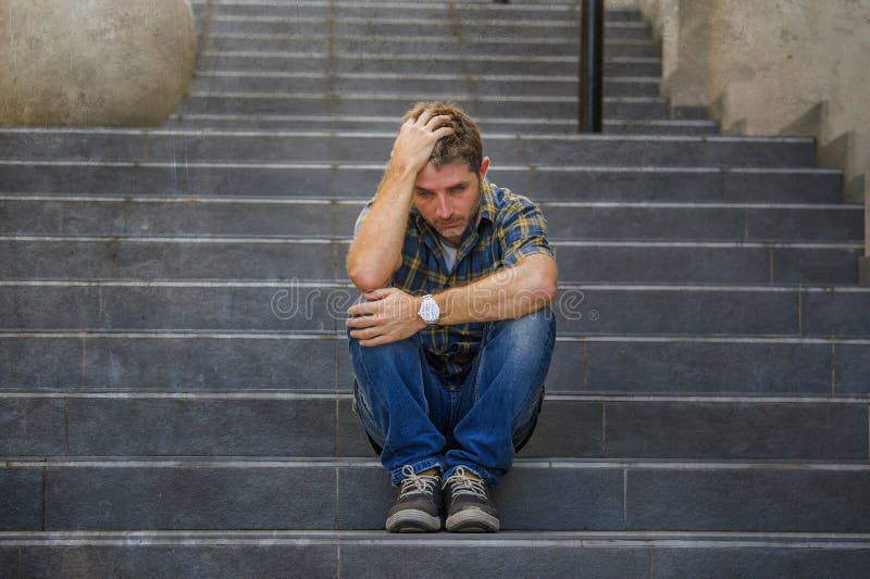 Junger trauriger und hoffnungsloser Mann, der draußen an der Straßentreppe erleidet elendes herein schreien des Angst- und Krisen