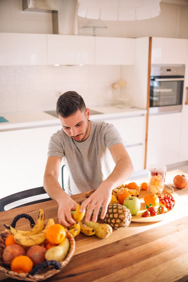 Young and healthy man putting fruits in his blender early in the morning. Young and healthy man putting fruits in his blender early in the morning