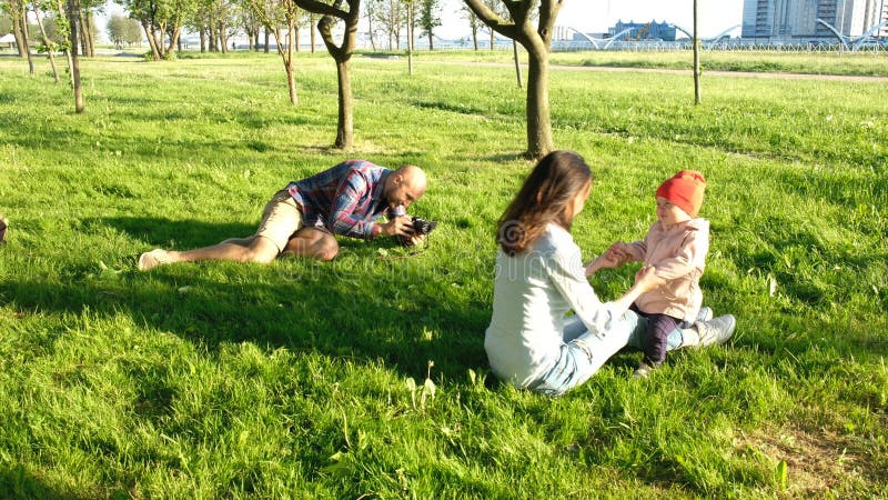 Junger Vater macht ein Foto einer kleinen Tochter mit ihrer Mutter im Park bei Sonnenuntergang Glückliche Familie geht in Natur lizenzfreie stockfotografie Junger Vater macht ein Foto einer kleinen Tochter mit ihrer Mutter im Park bei Sonnenuntergang Glückliche Familie geht in Natur lizenzfreie stockfotografie