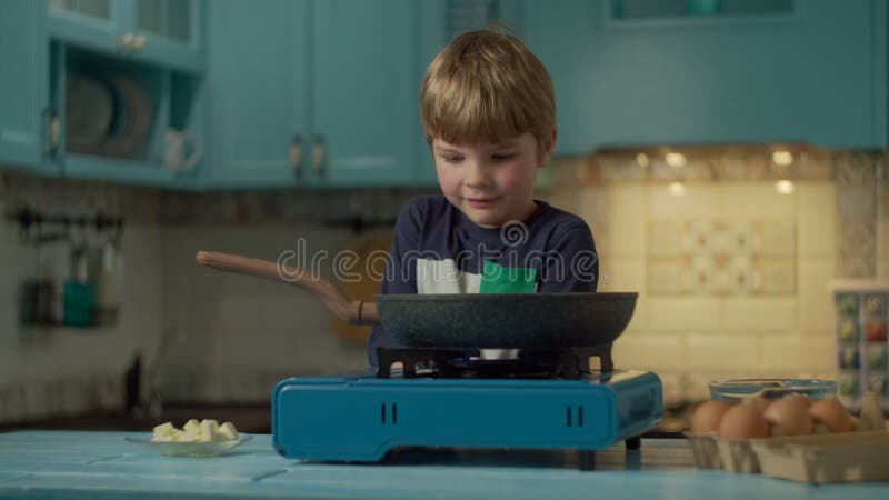 Junger Vorschuljunge, der allein die durcheinandergemischten Eier allein zu Hause stehen auf der blauen Küche kocht. Feuer der Kin stock footage