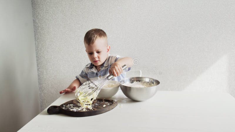 Junger Vorschuljunge, der allein Teig für den Kuchen allein zu Hause steht auf weißer Küche kocht. stock video