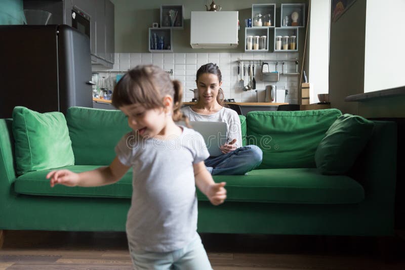 Junges allein erziehende Mutter, das Laptop während Tochterspielen verwendet lizenzfreie stockfotos
