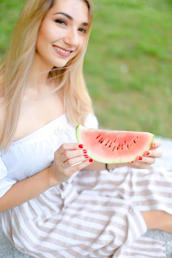 Junges amerikanisches Mädchen, das Wassermelone isst und Kleid, Gras im Hintergrund trägt