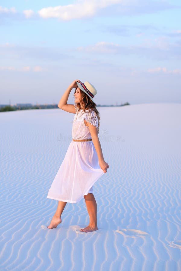 Junges amerikanisches Mädchen im weißen Kleid und im Hut, die auf Sand barefoo geht