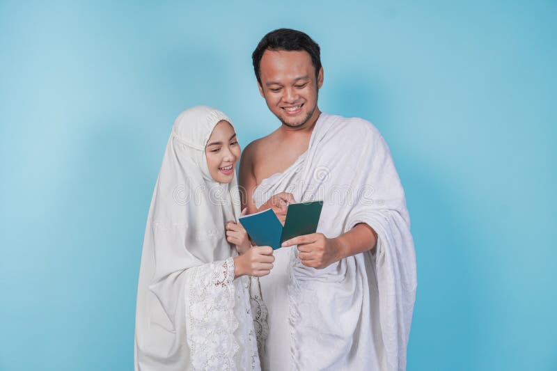 Junges asiatisches Muskelpaar im ihram und Gebetskleid, das sich gegenseitig Pass anschaut, isoliert von blauem Hintergrund. Hadsc lizenzfreies stockbild