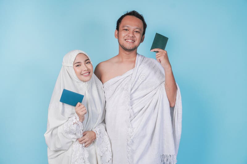 Junges asiatisches Muslimpaar, das ihram und Gebetspass trug, mit blauem Hintergrund abgeschirmt. Hadsch-Konzept stockbild