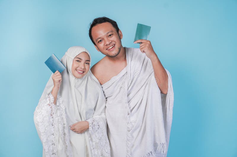 Junges asiatisches Muslimpaar, das ihram und Gebetspass trug, mit blauem Hintergrund abgeschirmt. Hadsch-Konzept stockbild