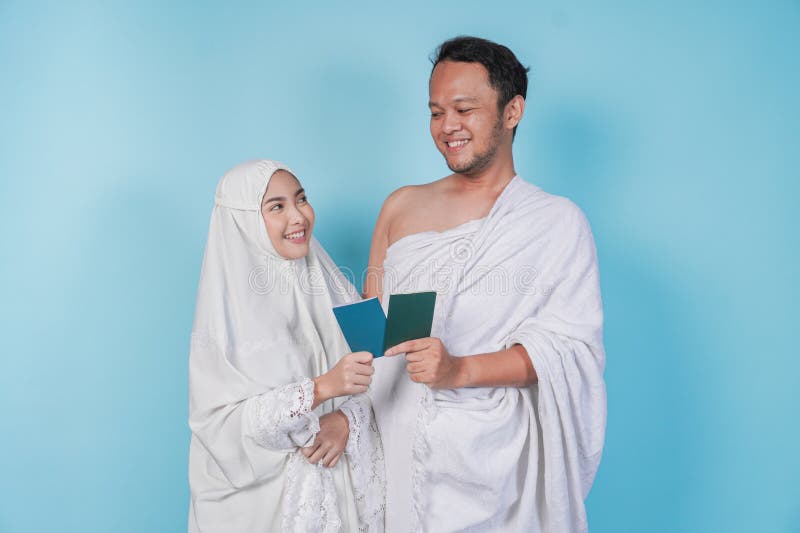 Junges asiatisches Muslimpaar im ihram und Gebetskleid mit Reisepass, während sie sich gegenseitig isoliert von blauem Hintergrund lizenzfreies stockfoto