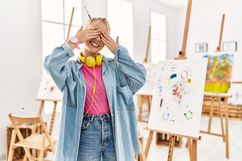 Young caucasian girl at art studio covering eyes with hands smiling cheerful and funny. blind concept. Young caucasian girl at art studio covering eyes with hands smiling cheerful and funny. blind concept