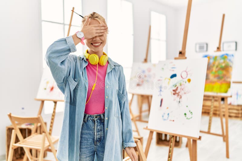 Young caucasian girl at art studio smiling and laughing with hand on face covering eyes for surprise. blind concept. Young caucasian girl at art studio smiling and laughing with hand on face covering eyes for surprise. blind concept