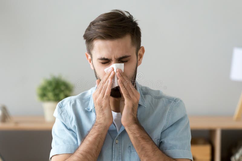 Junges krankes Mannholdingtaschentuch, das bei der Arbeit niest lizenzfreies stockbild Junges krankes Mannholdingtaschentuch, das bei der Arbeit niest lizenzfreies stockbild