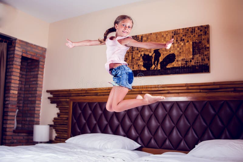 Junges Mädchen, das den Spaß springt auf Bett im Schlafzimmer hat stockfoto Junges Mädchen, das den Spaß springt auf Bett im Schlafzimmer hat stockfoto
