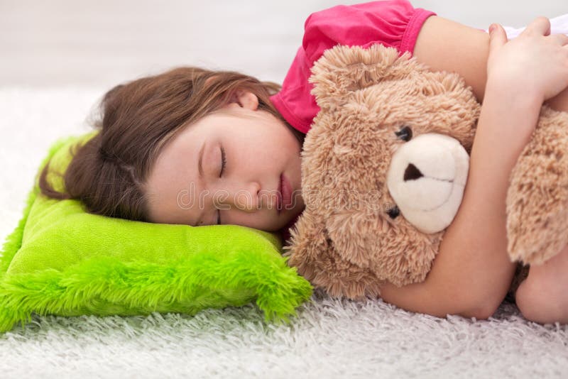 Junges Mädchen, das mit ihrem Teddybären ein Schlaefchen hält